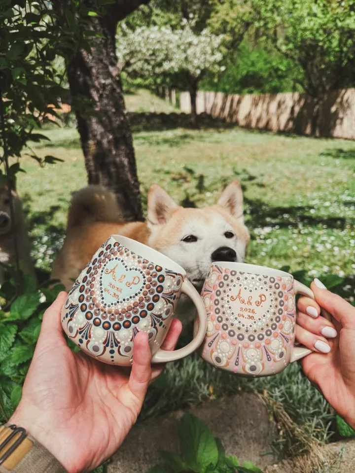 Két kézzel festett bögre A és P monogrammal és a 2026. 04. 30. dátummal, mögöttük Góré, a shiba inu